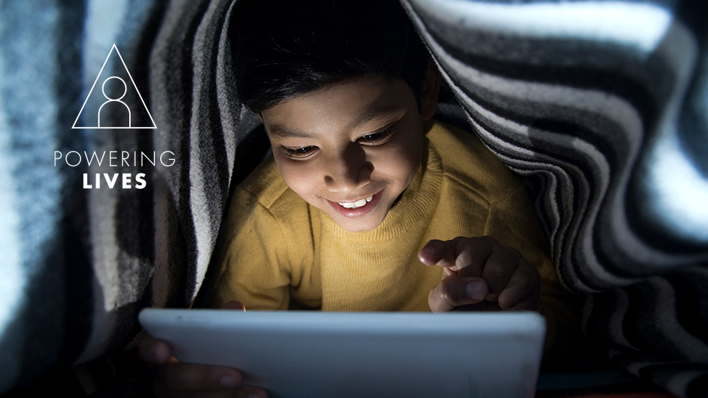 Young boy smiling and reading on a tablet under a blanket  (photo)