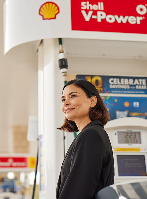 Woman smiling, standing by her car in a Shell retail site, USA. (photo)