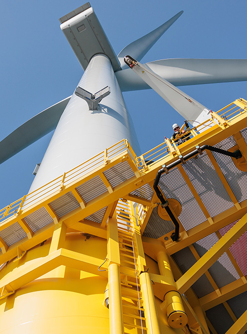 Wind turbine pictured from the sea looking up at an employee standing on a platform half way up. (photo)
