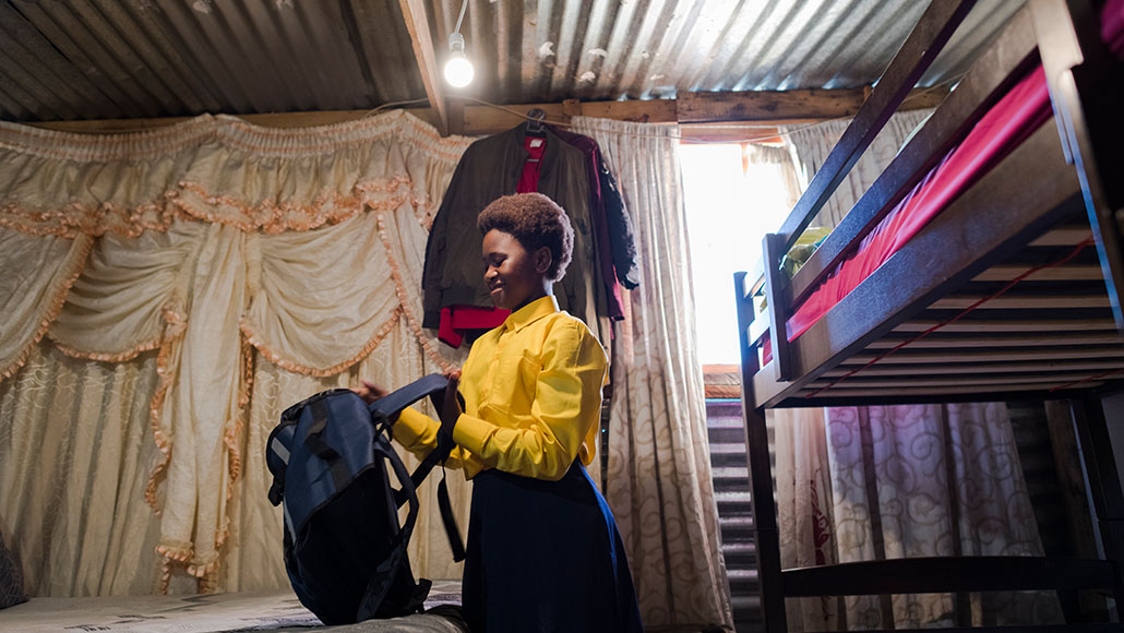 schoolgirl packing her backpack in a hut with a corrugated iron roof which is lit by a light bulb (photo)