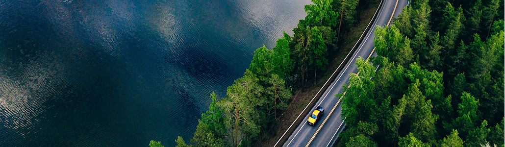 Aerial view of a lane with two cars going through a forest beside a lake (photo)
