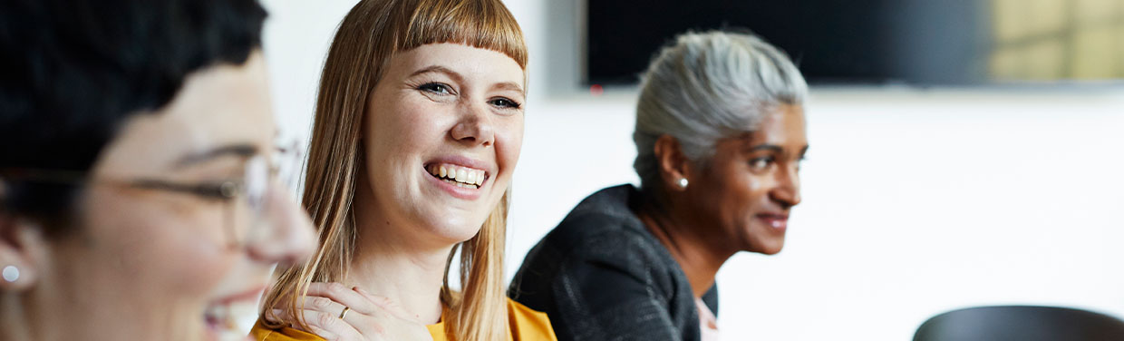 Woman smiling in business meeting, another woman in the background (photo)