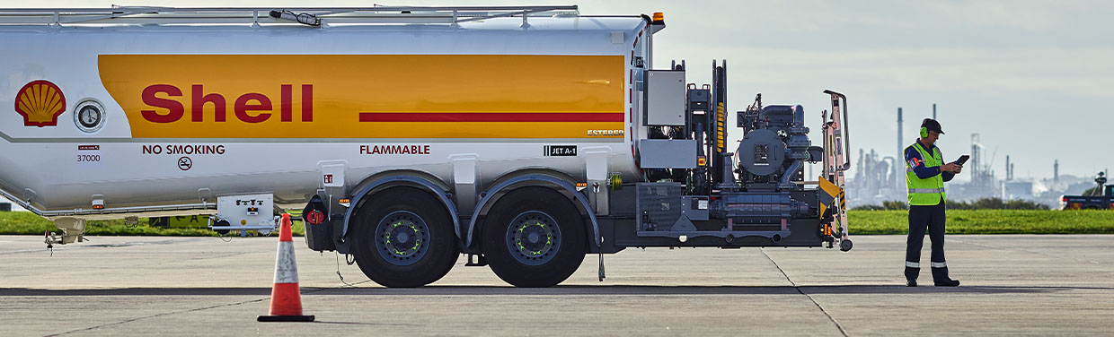 Shell employee in high-visibility clothes standing in front of a Shell road tanker at the airport (photo)