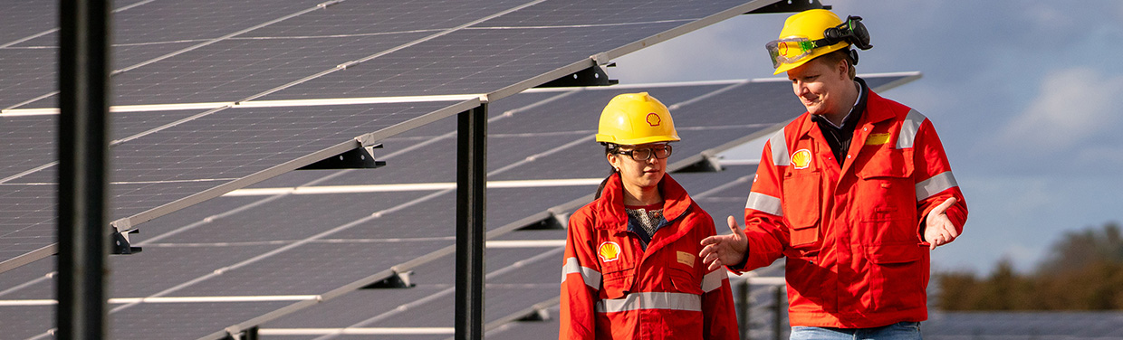 Two Shell employees with protective clothes talking in front of solar panels (photo)