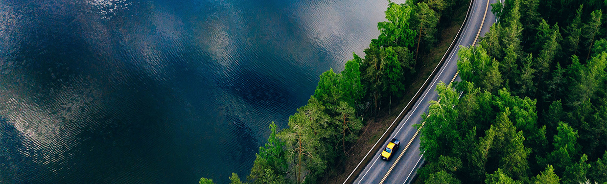Aerial view of a road with two cars going through a forest next to a lake (photo)