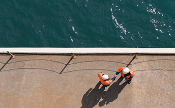 Aerial view of two man in PPE shaking hands at the edge of the harbour
