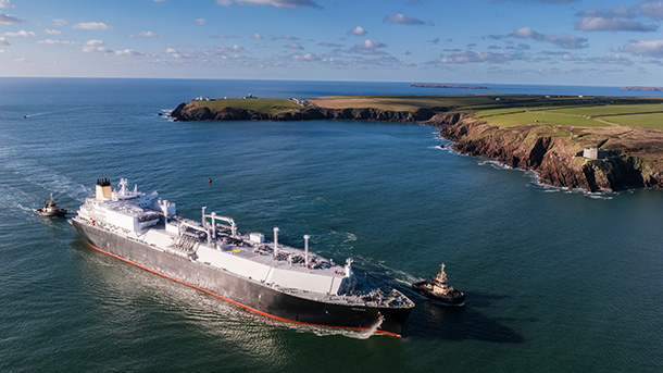 Aerial view of a large ship passing by cliffs and green fields
