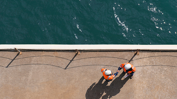 Aerial view of two man in working clothes and helmets shaking hands at the edge of the harbor