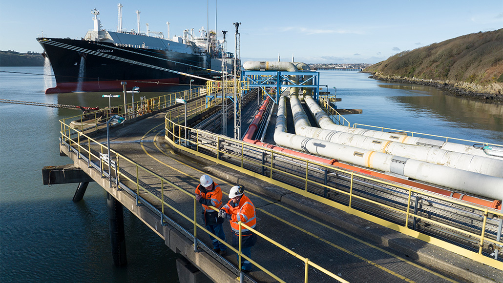 LNG tanker berthed next to pipeline with two Shell employees in the foreground