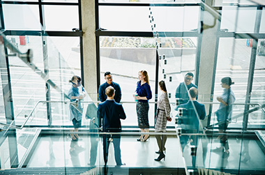 A group of colleagues standing in a glass office environment having an informal meeting