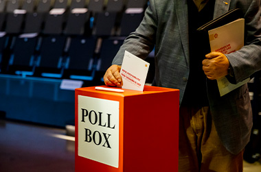 Photo showing a poll box with a person inserting a ballot