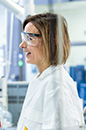 Two people in a laboratory wearing safety goggles and Shell lab coats smiling at each other. (photo)