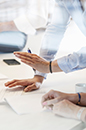 Image of meeting showing multiple hands handling papers on table. (photo)