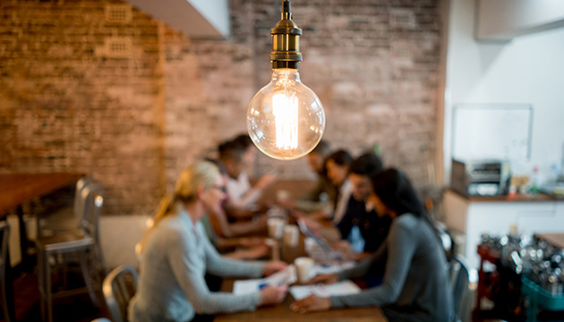 Lightbulb hanging with people having a meeting around a table in the background. (photo)