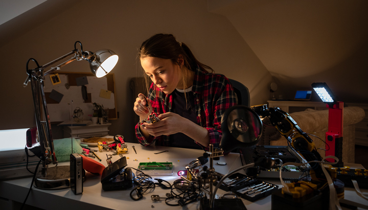Teenage girl sitting at her desk in her bedroom working with some electronic components, UK, 2019 (photo)