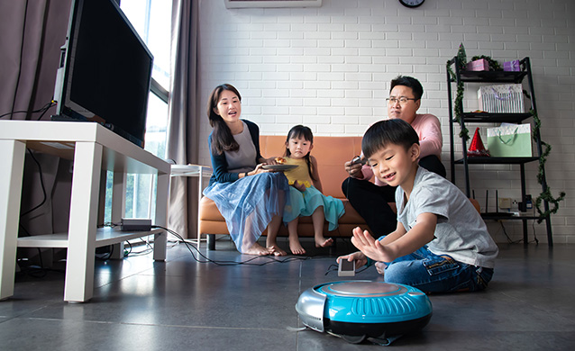Cheerful family having leisure moment in their living room and letting the robotic vacuum cleaner do the cleaning, Malaysia, 2019 (photo)