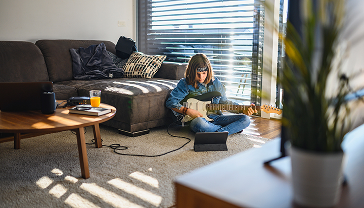 Young boy playing guitar in a living room, using a digital tablet. (photo)