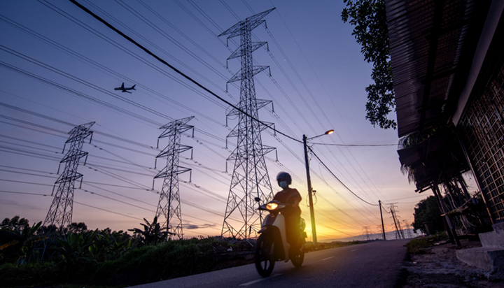 A person riding motorcycle on road in Malaysia at sunset, beside electrical transmission towers with a plane flying overhead. (photo)