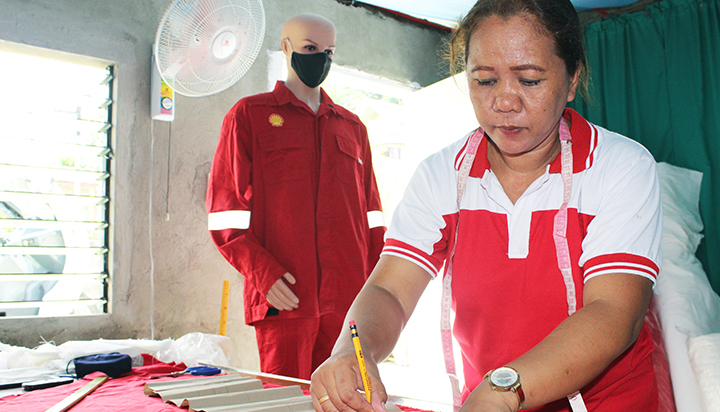 A woman cutting fabric, with a mannikin wearing Shell coveralls in the background, in the Philippines. (photo)