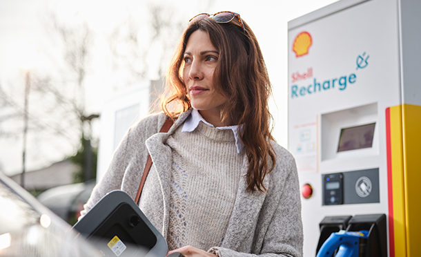 Woman in front of a Shell electric vehicle charging station (photo)