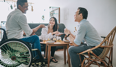 Two men, one in a wheelchair, and a woman laughing while having tea and cake (photo)