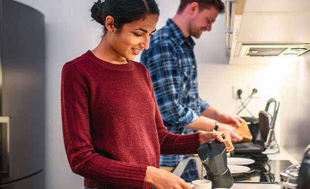 Happy young multi-ethnic couple using energy for cooking and preparing coffee in kitchen. Europe. (photo)