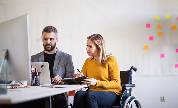 Woman using wheelchair looking at computer with male colleague (photo)