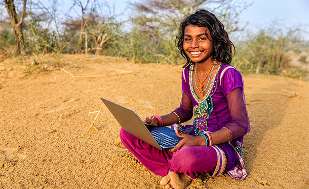 A girl in india sits on the ground smiling with a laptop computer (photo)