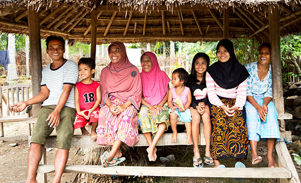 A muslim family sit on the steps of a basic bamboo hut laughing together (photo)