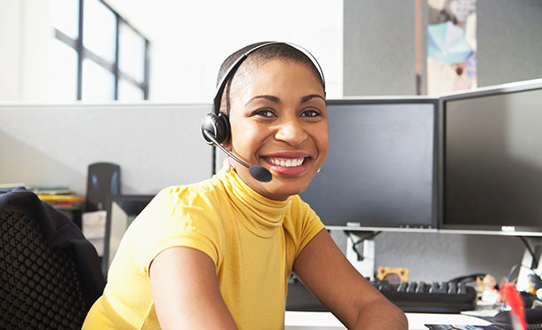 Smiling employee sitting at a desk using phone headset and computer (photo)