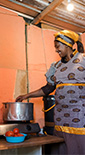Woman happily cooking at home using electric cooker and fridge, in Africa (photo)