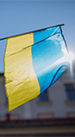 Person holding the Ukraine flag with a building and the sun behind it (photo)