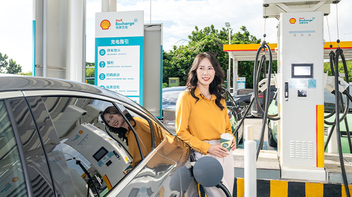 A smiling woman is at an electric car charging station with a coffee cup in hand (photo)