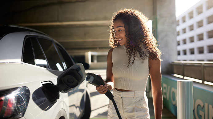 Young woman with curly hair holding electric plug by car at charging station
(photo)