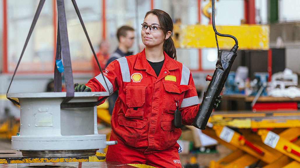 Shell female employee working on-site and handling heavy equipment, wearing red branded workwear (photo)