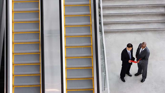 Two men shaking hands and talking in an office foyer alongside a staircase (photo)